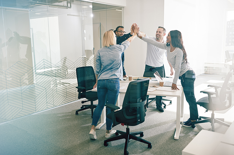 Smiling colleagues standing together around an office table high fiving