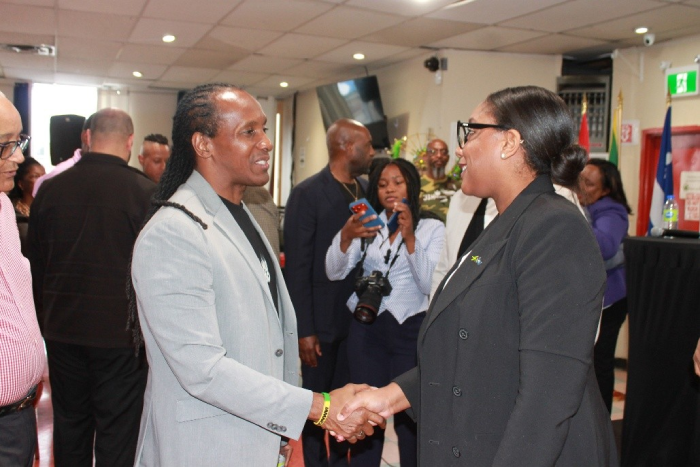 Two professionals shake hands at a formal event, with photographers and attendees in the background.