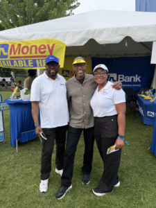Three people stand together outdoors at a booth under a white tent, smiling for the camera with bank banners in the background.