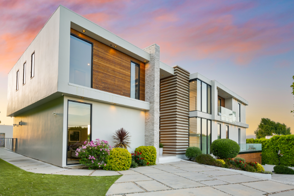 Modern two-story house with clean lines, white and wood facade, glass balconies, and a stone pathway at sunset.